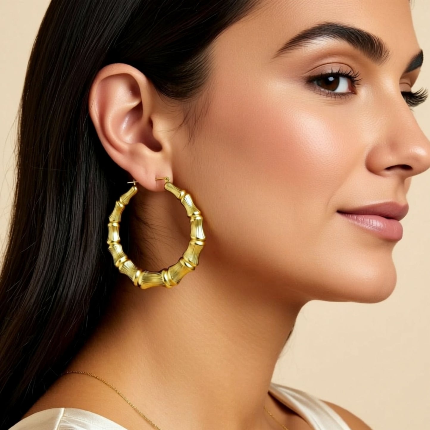 Woman wearing bamboo gold hoop earrings with a neutral background